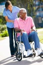 Carer Pushing Senior Man In Wheelchair