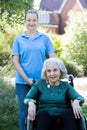 Portrait Of Carer Pushing Senior Woman In Wheelchair Outside Home