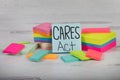 CARES ACT hand written on blue posted note blank sticky notes piled up and stacked on a white wooden background