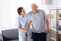 Caretaker Assisting Senior Man While Walking At Home