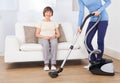 Caretaker cleaning floor while senior woman sitting on sofa