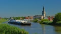 Cargo ship on river Scheldt with church tower in the flemish countryside
