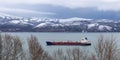 Cargo ship sails along the sea Bay against the background of snow-capped mountains. Royalty Free Stock Photo