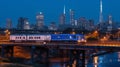 Cargo train crossing river with city skyline at blue hour Royalty Free Stock Photo