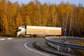 A cargo van drives on a highway against the backdrop of a yellow birch forest in autumn