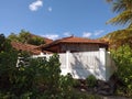 Caribbean colonial house surrounded by lush vegetation. Roof and shutters in tropical residence with white garden fence under blue Royalty Free Stock Photo