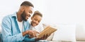 Caring african-american daddy reading book to his cute daughter Royalty Free Stock Photo