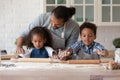 Caring African American father teaching kids rolling out dough