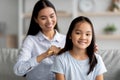 Caring asian mother brushing her cute daughter hair while sitting together on sofa at home in living room interior Royalty Free Stock Photo