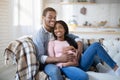 Caring black man embracing his pregnant wife on sofa at home Royalty Free Stock Photo