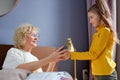 Caring child girl giving cup of tea to granny sitting on bed in cozy room, family love