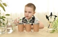 A caring child sprays with water from a grown green cucumber sprouts in cups. Home gardening. Cultivation of plants.