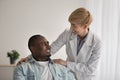 Happy adult woman nurse helping to smiling middle aged african american guy disabled in wheelchair