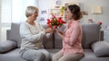 Caring elderly mother presenting gift and tulips to daughter at birthday, love