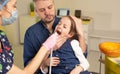 a caring father helps the dentist to support the child during the dental procedure on children's teeth.