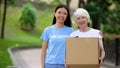 Caring female activist hugging old woman donation card box, social volunteering Royalty Free Stock Photo