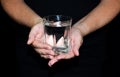 Caring female hands holding a glass of water on a black backgrou