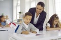 Caring friendly female teacher helps little boy with school assignment in class. Royalty Free Stock Photo