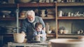 Caring grandfather experienced potter is teaching little boy how to work with clay on potter& x27;s wheel. Grandson is Royalty Free Stock Photo