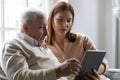 Caring grownup daughter teaching elderly father to use tablet