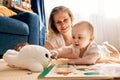 Caring joyful mother plays with her little child, lying on the floor in a bright children's room. Various toys, a Royalty Free Stock Photo