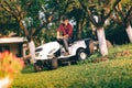 Caring lawncare concept - handsome young man trimming grass in garden using tractor