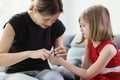 Caring mommy cuts off nails of daughter sitting on sofa