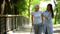 Caring nurse helping senior disabled woman with frame walk in park, rehab Royalty Free Stock Photo