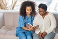 Caring nurse sitting on sofa near patient and reading book for her Royalty Free Stock Photo