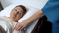 Caring nurse supporting desperate elderly patient lying in hospital bed, disease