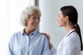 Caring nurse touching smiling older woman shoulder, expressing support