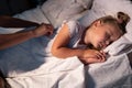 Caring parent mom put blanket on sleeping little girl daughter on bed in dark bedroom at night. Loving mother take care