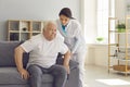 Friendly female doctor helps an older man who is trying to get up from the couch. Royalty Free Stock Photo