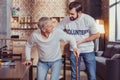 Caring pleasant volunteer standing and helping retired. Royalty Free Stock Photo