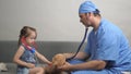 Caring professional male pediatrician playing with small child in room. Little girl plays with a teddy bear Teddy Royalty Free Stock Photo