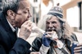 Caring short-haired business man and poor old man biting pieces of sandwich