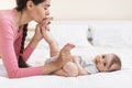 Caring young mother kissing baby& x27;s feet while making gymnastics on bed at home, side view, copy space Royalty Free Stock Photo