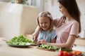 Caring young mom teach little daughter chop vegetables