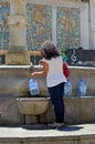 Lady filling water bot;e, Street scene in Carini Sicily Italy