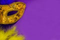 Carnival. Festive background with copy space. Golden carnival mask with blue and yellow feathers on a purple background. Mardi