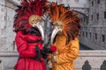 Costumed carnival-goers with red feathered mask standing in by the Bridge of Sighs during Venice Carnival Carnivale di Venezia. Royalty Free Stock Photo