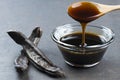 Carob molasses in glass bowl and in wooden spoon and carob pods on rustic background