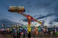 Carousel with many lights turns fast in front of steady spectators