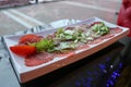 Carpaccio of red beef and pork with tomatoes sprinkled with cheese and greens on a white rectangular plate on a table in a cafe Royalty Free Stock Photo