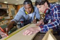 carpenter with apprentice using retractable tape-measure in workshop