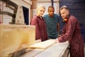 Carpenter With Apprentices Using Circular Saw In Workshop