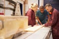 Carpenter With Apprentices Using Circular Saw In Workshop