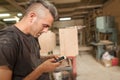 Carpenter artisan resting in workshop and scrolling on smartphone