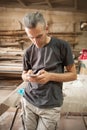 Carpenter artisan resting in workshop and scrolling on smartphone