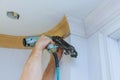 Carpenter brad using nail gun to Crown Moulding framing trim, with the warning label that all power tools